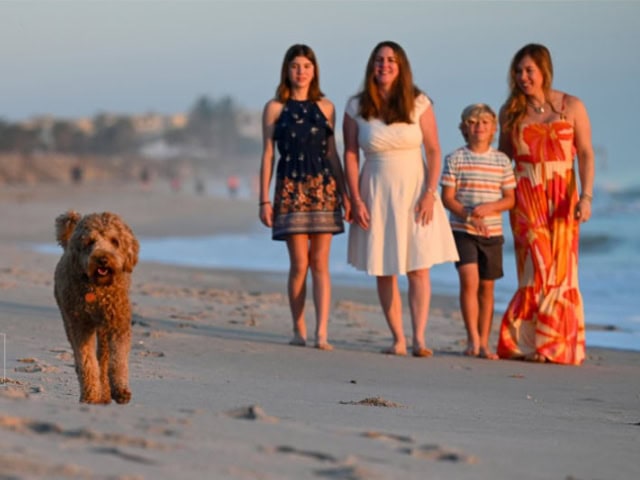 A woman and children walking on the beach with a dog, sunset scene.