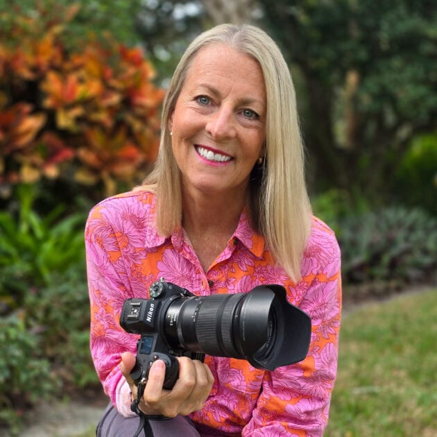A woman holding a professional camera outdoors in a garden setting.
