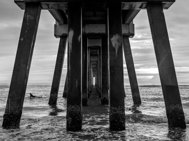 A pier extending into the ocean with wooden supports and a cloudy sky.