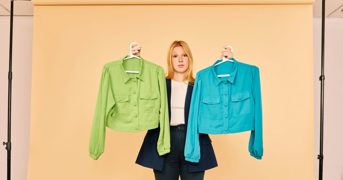 A woman holding two colorful jackets for a professional headshot, neutral background, fashion choice.